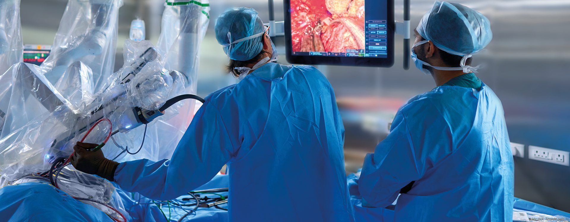 Zwei Personen in blauer OP-Kleidung in einem Da-Vinci-Operationssaal. Eine Person hält ein Endoskop in den Operationssitus. Beide Personen betrachten das vom Endoskop auf den Monitor projezierte Bild vom OP-Bereich.