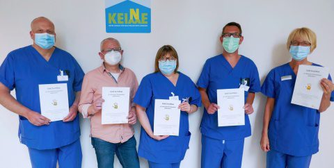 Fünf Personen und größtenteils blauer Krankenhauskleidung halten Zertifikate der "Aktion Saubere Hände" vor sich.