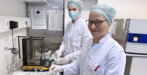 Foto von zwei Mitarbeitern der Zentralapotheke. Pharmaziestudentin Kristina Adrian mit weißem Kittel lächelt während einer Tätigkeit in die Kamera.