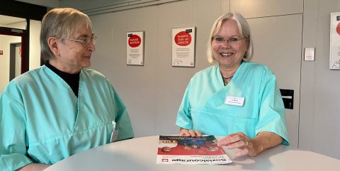 Zwei ehrenamtlich tätige Damen stehen an einem Tisch.