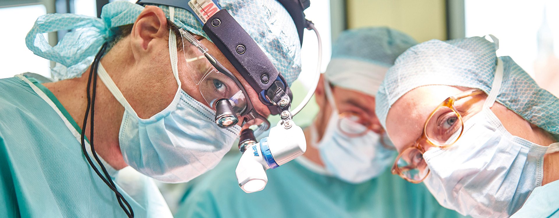 OP-Situation, drei Personen in grüner =P-Arbeitskleidung während einer Operation