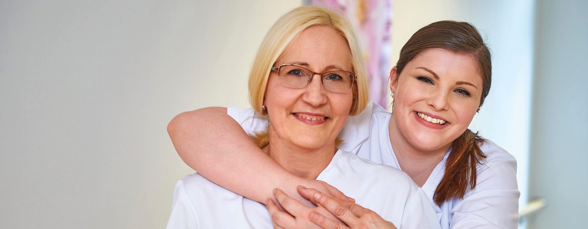 Zwei lächelnde weibliche Pflegekräfte in weißer Krankenhausarbeitskleidung