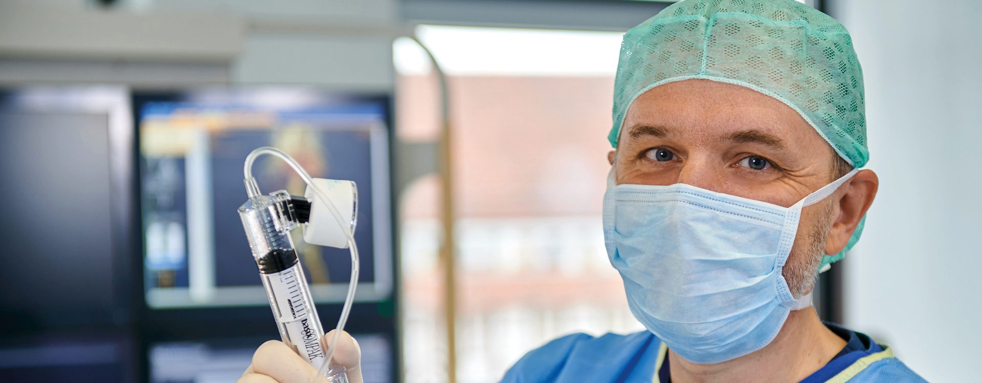 männliche Person in blauer OP-Arbeitskleidung mit Mundschutz und OP-Haube