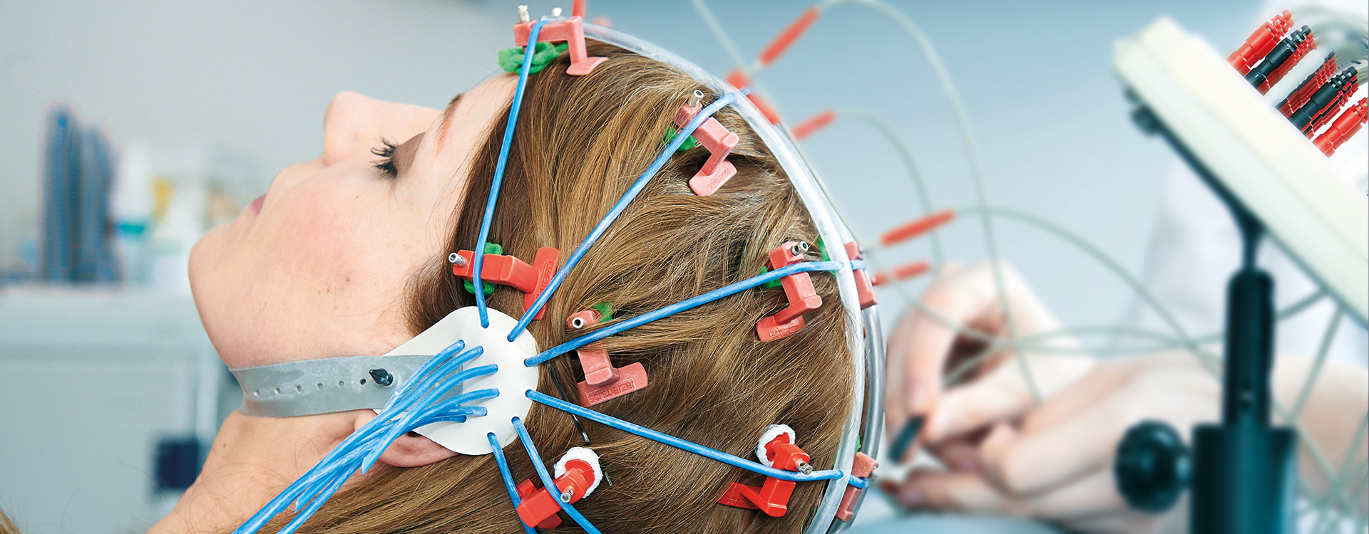 Frau während einer EEG-Untersuchung auf dem Untersuchungsstuhl mit Elektroden am Kopf